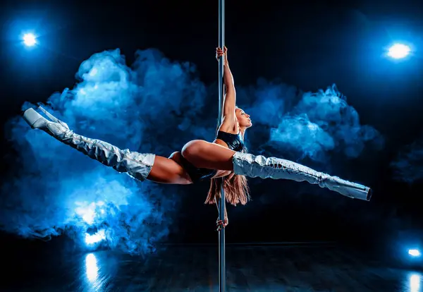 Young woman pole dancing on dark background with blue smoke and lights