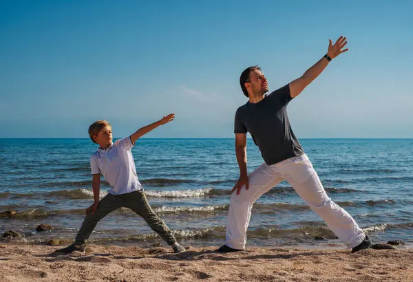 Father and son doing sports exercises on the beach at summer day