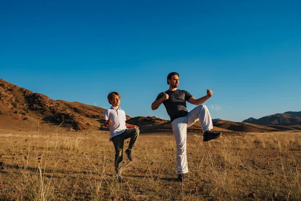 Father and son doing sports exercises on mountains background