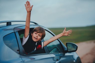 Arabanın camından sarkan mutlu çocuk.