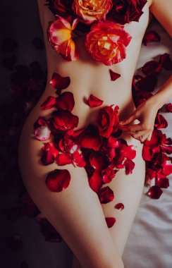 Güzel bir kadın gül yapraklarıyla yatakta yatıyor.