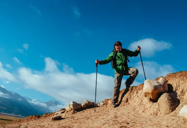 Man hiker with trekking poles climbing down from rocks
