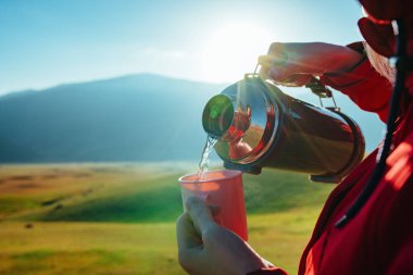 Dağlardaki kadın turist termostan fincana çay döküyor.