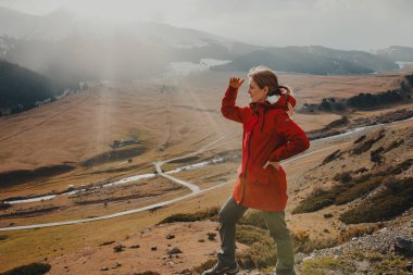 Genç bayan turist dağın tepesinde duruyor ve başka tarafa bakıyor.