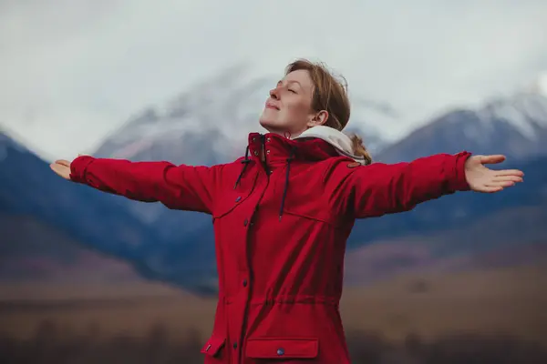Happy woman tourist standing on mountains background with arms out