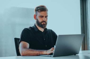 Ofiste dizüstü bilgisayarda çalışan genç adam.