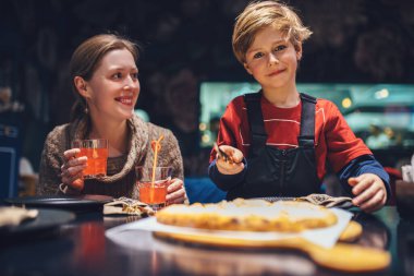 Annesiyle kafede pizza yiyen mutlu bir çocuk.