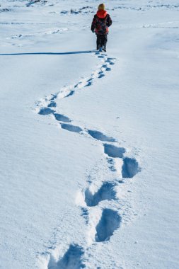 Çocuk karda kar yığınlarında yürür ve ayak izleri bırakır.