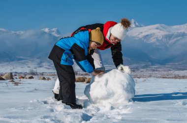 Mutlu anne ve oğul dağlarda kardan adam yapıyor.