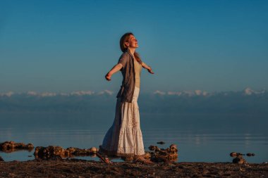 Güzel genç bir kadın göl kenarında gözleri kapalı yürüyor.