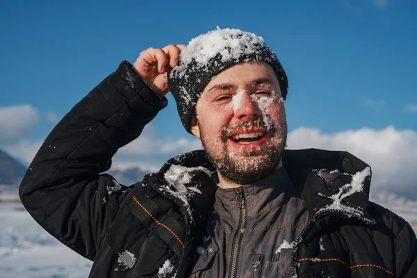 Młody Uśmiechnięty Mężczyzna Śniegiem Twarzy Portret Tle Gór Zimie — Zdjęcie stockowe