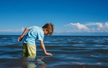 Çocuk gölde duruyor ve su yüzeyine dokunuyor.