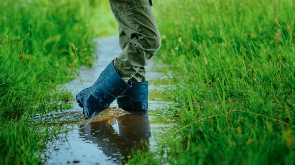 Boy in rubber boots walking on small stream on summer field