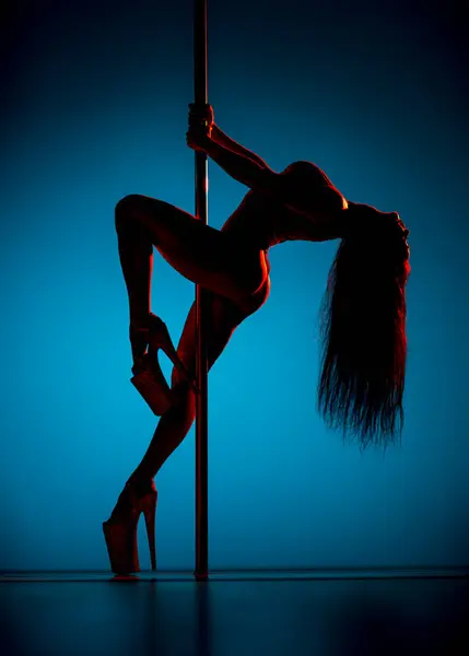 Young sexy woman pole dancing in blue and red neon lights, tattoo on body
