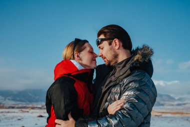 Kışın dağların arka planında kucaklaşan romantik genç çift