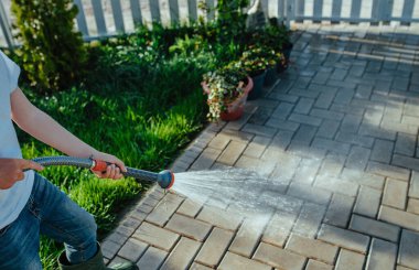 Oğlan yazın bir hortumdan çıkan su jetiyle geçidi temizliyor.