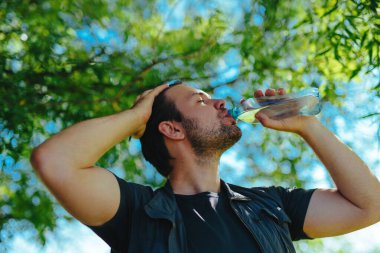 Sıcak yaz gününde ağacın altındaki şişeden saf su içen adam.