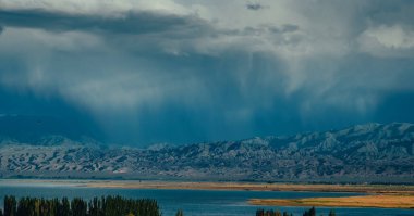 Dağların üzerinden yağmur bulutları ve yazın göl manzarası.