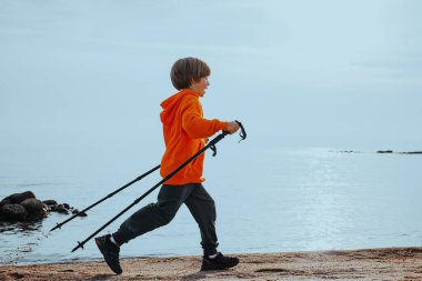 Göl kıyısında yürüyüş direğiyle koşan mutlu çocuk yürüyüşçü.