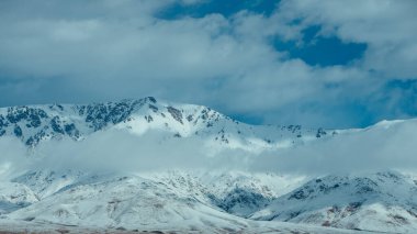 Bulutlu havada karlı dağ tepeleri olan güzel bir manzara.