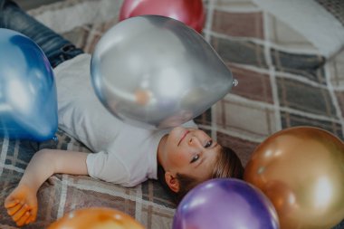 Balonlarla yatakta uzanan tatlı çocuk portresi. Kutlama konsepti.