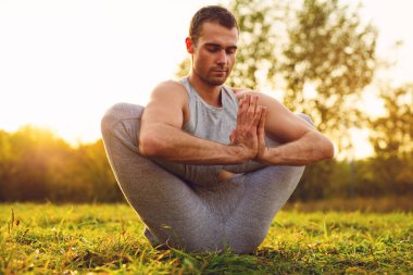 Yogi adam yaz günü parkta antrenman yapıyor, sıcak gün batımı ışığı.