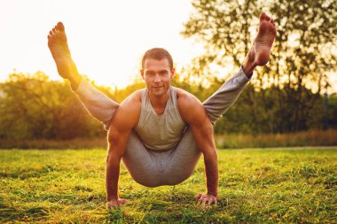Yogi adam yaz günü parkta antrenman yapıyor, sıcak gün batımı ışığı.