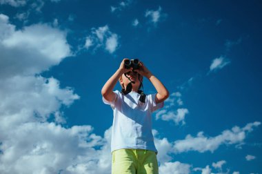 Mavi gökyüzü arka planında dürbünle bakan çocuk portresi