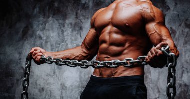 Arka planda ağır zincirli, güçlü bir vücut geliştiren genç adam.
