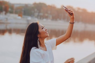 Güneşli bir sabahta nehir geçmişinde selfie çeken genç bir kadın.