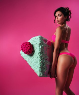 Pembe arka planda koca bir dilim pastası olan iç çamaşırlı zayıf bir kadın.