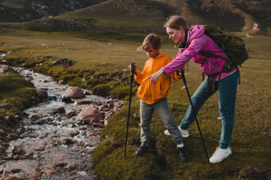Oğluyla birlikte dağ vadisinde akarsu boyunca yürüyen genç bir turist.