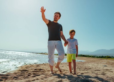 Baba ve oğul yaz günü göl kıyısında yürüyorlar.