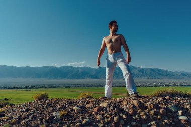 Genç, güçlü, üstsüz adam yaz günü dağda dikiliyor.