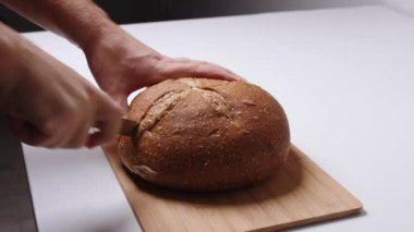 Beyaz masa manzaralı tahta üzerinde ekmek kesen bir adam.