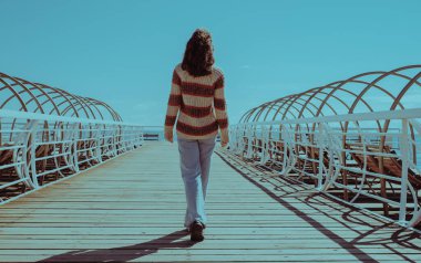 Deniz kıyısında köprüde yürüyen genç kadın, kıç manzaralı.