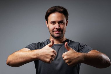 Man portrait showing thumbs up on gray wall background clipart