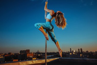 Alacakaranlıkta çatıda dans eden genç ve zayıf bir kadın.