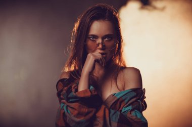 Gözlüklü genç kadın stüdyo resmi, sıcak renkler.