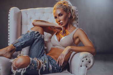 Sandalyede oturan genç bir kadın. Stüdyo resmi, elinde dövme.