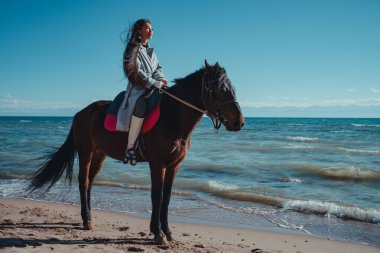 Genç Asyalı kadın yaz günü göl kıyısında ata biniyor.