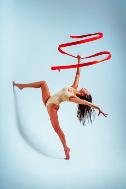 Beyaz arka planda kırmızı kurdeleyle dans eden genç bayan jimnastikçi.