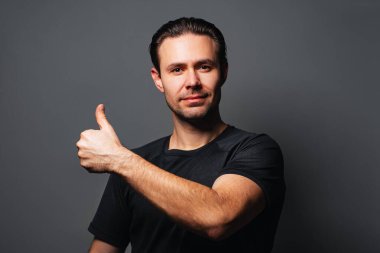 Gri arkaplanda baş parmakları gösteren adam portresi