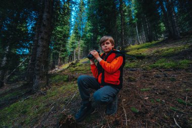 Dürbünlü çocuk turist dağlardaki karanlık vahşi ormanda oturuyor.