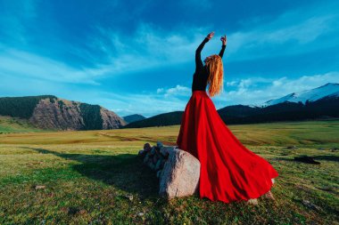 Yüksek dağlarda duran kırmızı elbiseli güzel kadın dansçı.