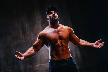 Taş duvar arkasında kaput portresi giymiş güçlü genç bir vücut geliştirici.