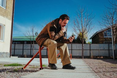 Adamın biri caddede park yerinde oturuyor ve telefona bakıyor.