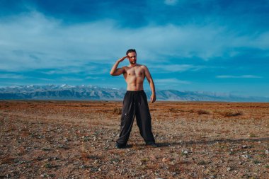 Genç ve güçlü bir adam dağlarda spor eğitimi alıyor ve selam veriyor.