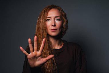 Gri arkaplandaki portrede dur hareketi gösteren genç bir kadın.