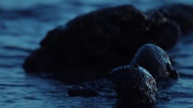 Alacakaranlıkta göl kıyısındaki taşların ve dalgaların yakın görüntüsü